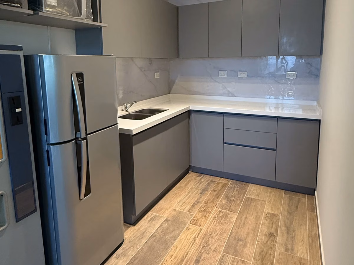 Cocina de oficina con muebles grises, mesada clara y heladera de acero.