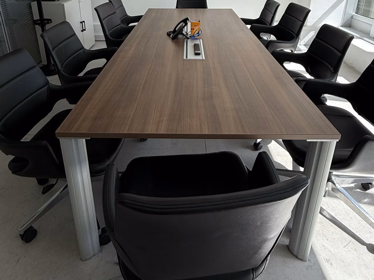 Mesa de reuniones en tono madera rodeada de sillas negras con apoyabrazos