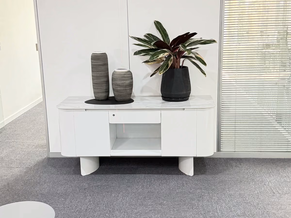 Mueble auxiliar blanco con puertas, estante central, jarrones y una planta